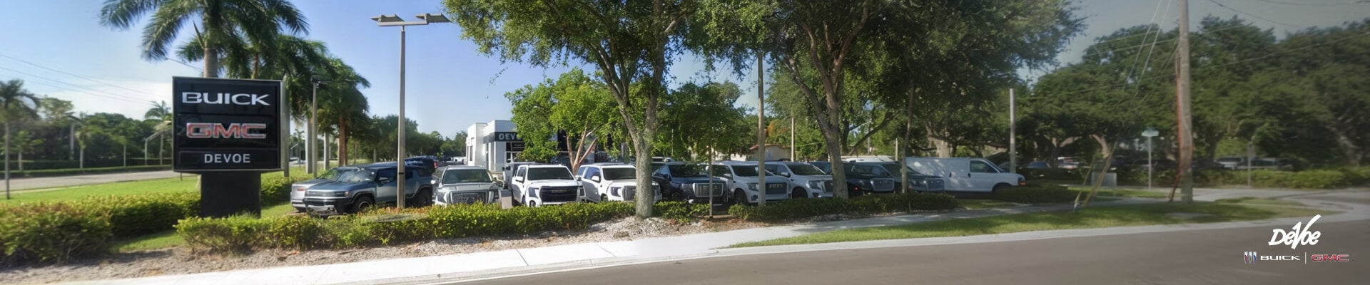 Wide angle view of DeVoe Buick and GMC dealer showcasing a lineup of modern SUVs and an electric pickup truck parked.