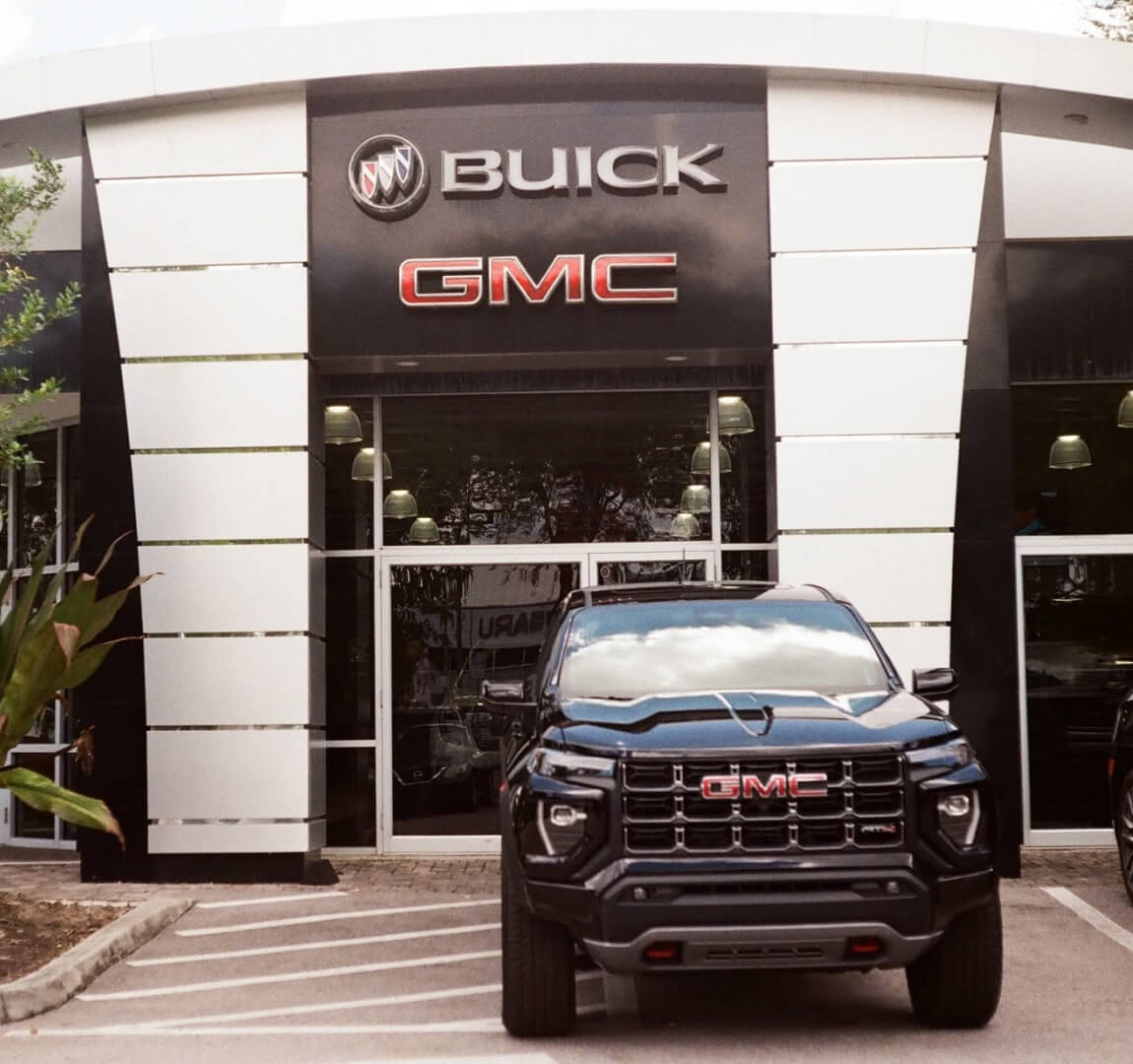Front view of a GMC Canyon AT4 in Onyx Black parked directly in front of the DeVoe Buick GMC dealership entrance.