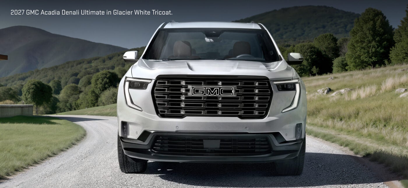 Front view of a 2027 GMC Acadia Denali Ultimate in White Frost Tricoat featuring a dark chrome grille on a gravel country road.