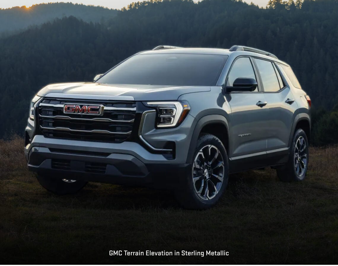 GMC Terrain Elevation parked on a grassy field overlooking a forested mountain.