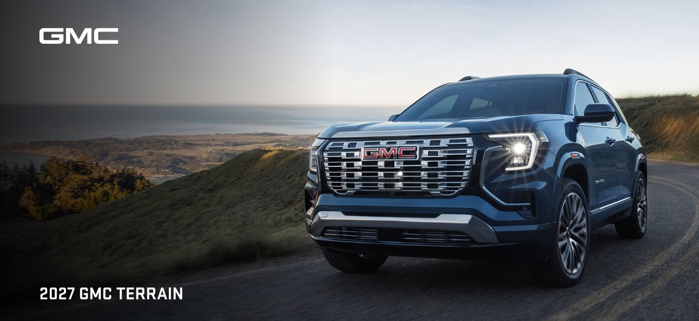 Front three-quarter view of a blue 2027 GMC Terrain Denali on a scenic coastal road.