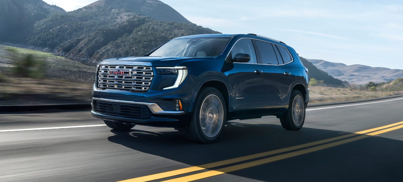 GMC vehicle with chrome grille driving on a scenic mountain road, conveying a sense of adventure and freedom.